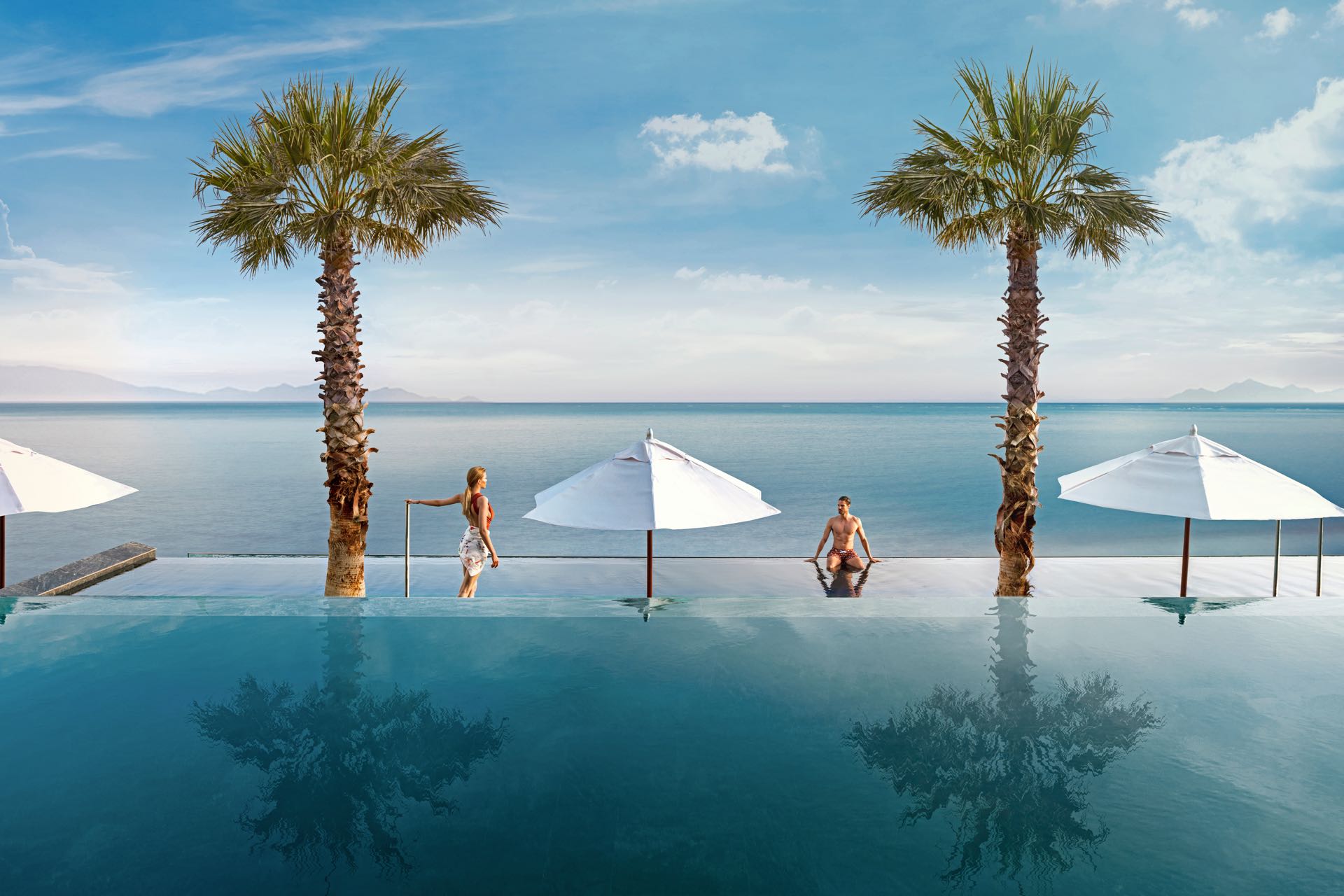 Koppel ontspant in een infinity pool met uitzicht op de oceaan en tropische palmbomen tijdens een romantische reis.